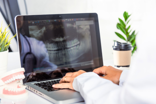 A dentist views an oral x-ray on a laptop. 