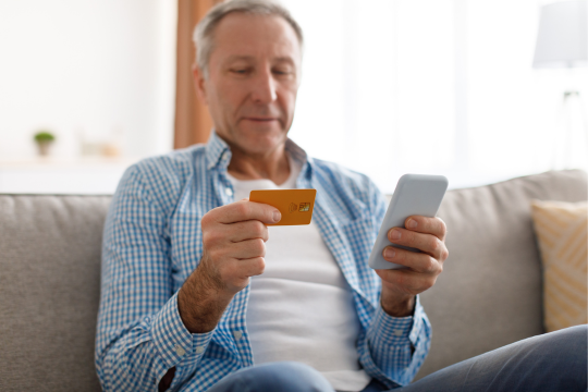Homme adulte tenant un téléphone intelligent et une carte de crédit.